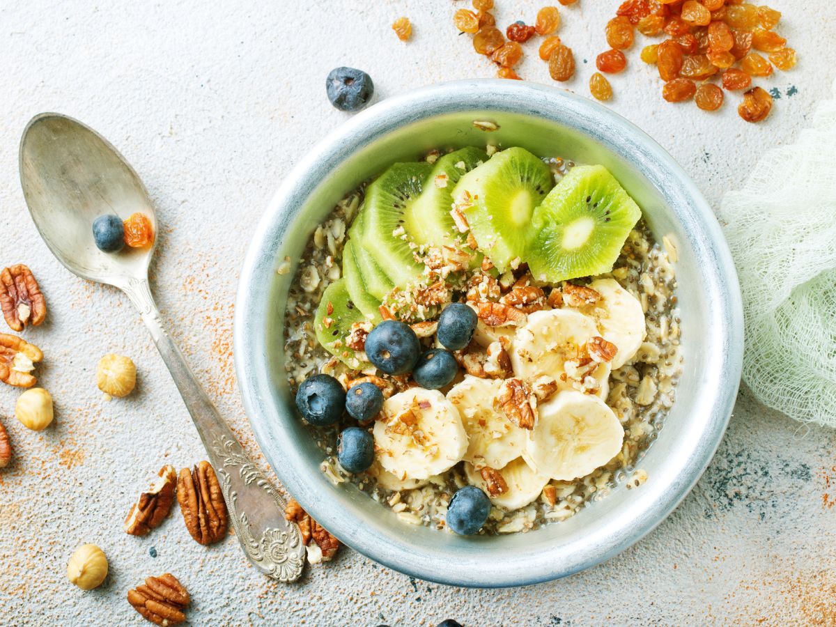 Photo of a breakfast bowl with oatmeal, banana, kiwi, blueberries, chia seeds, and pecans.