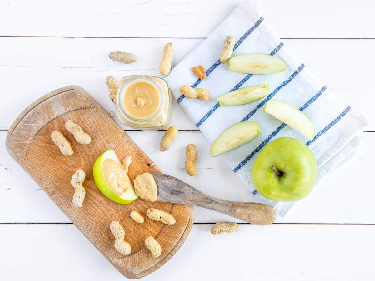 Apple slices with peanut butter and peanuts on a cutting board.