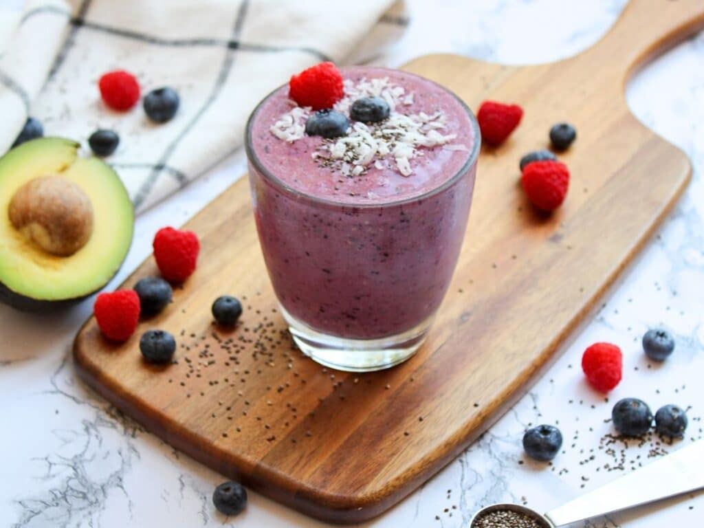 berry avocado fertliity smoothie on top of a wood cutting board with avocado and berries in the background.
