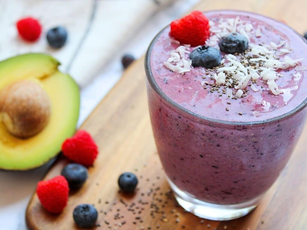 berry avocado fertliity smoothie on top of a wood cutting board with avocado and berries in the background.