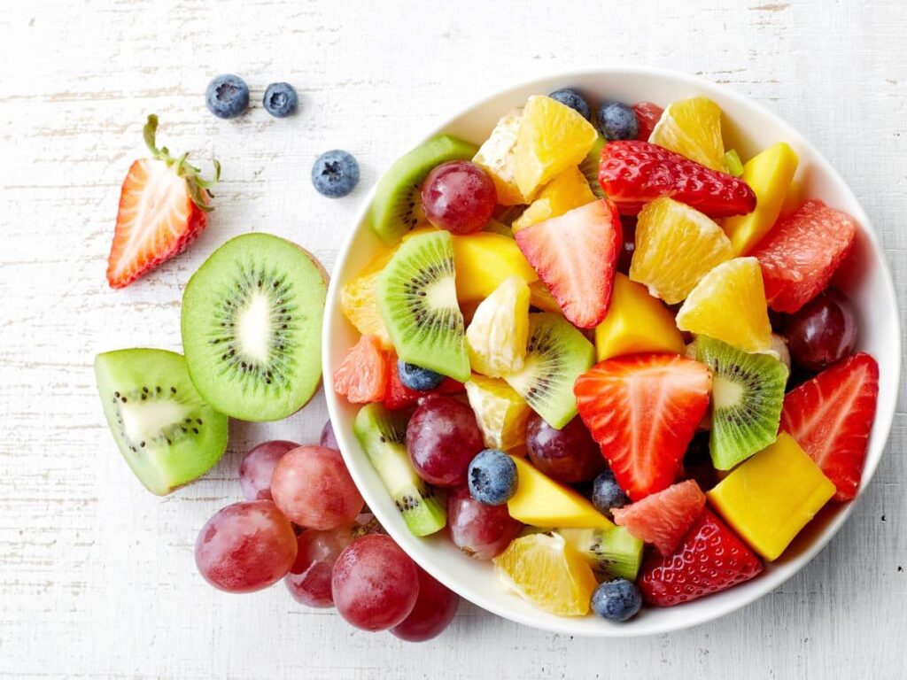 Bowl of fruit on a table with miscellaneous fruit on tabletop.