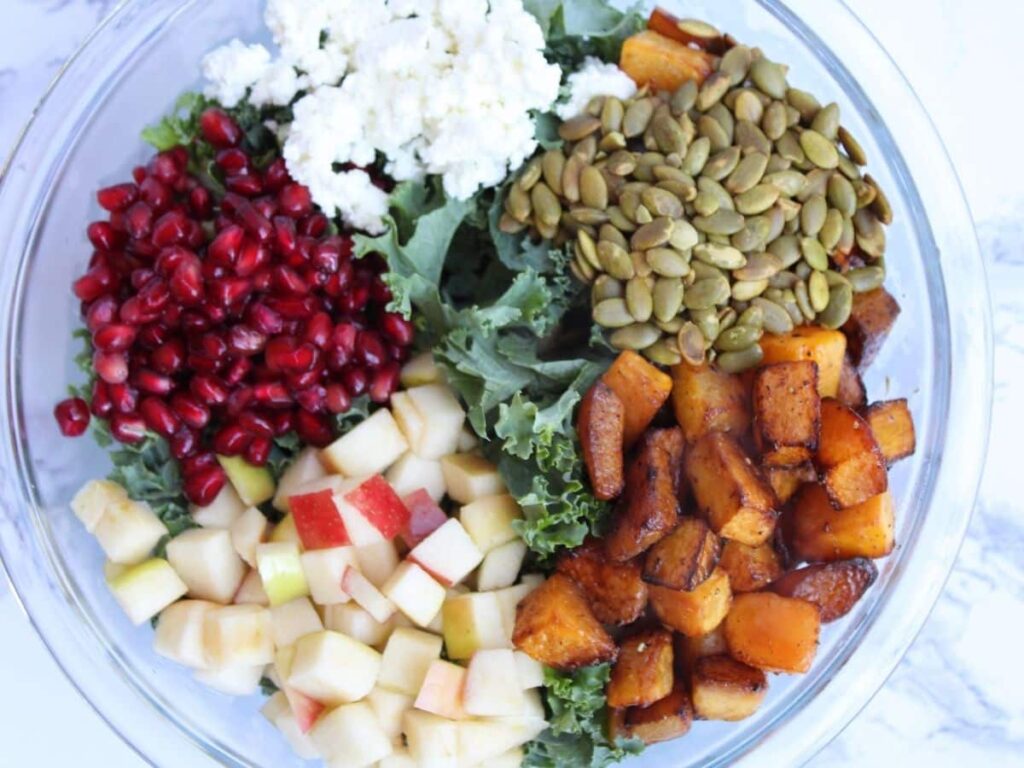 Closeup photo of a fall kale salad with butternut squash, goat cheese, pomegranate seeds, pepitas, and apple prior to it being mixed up