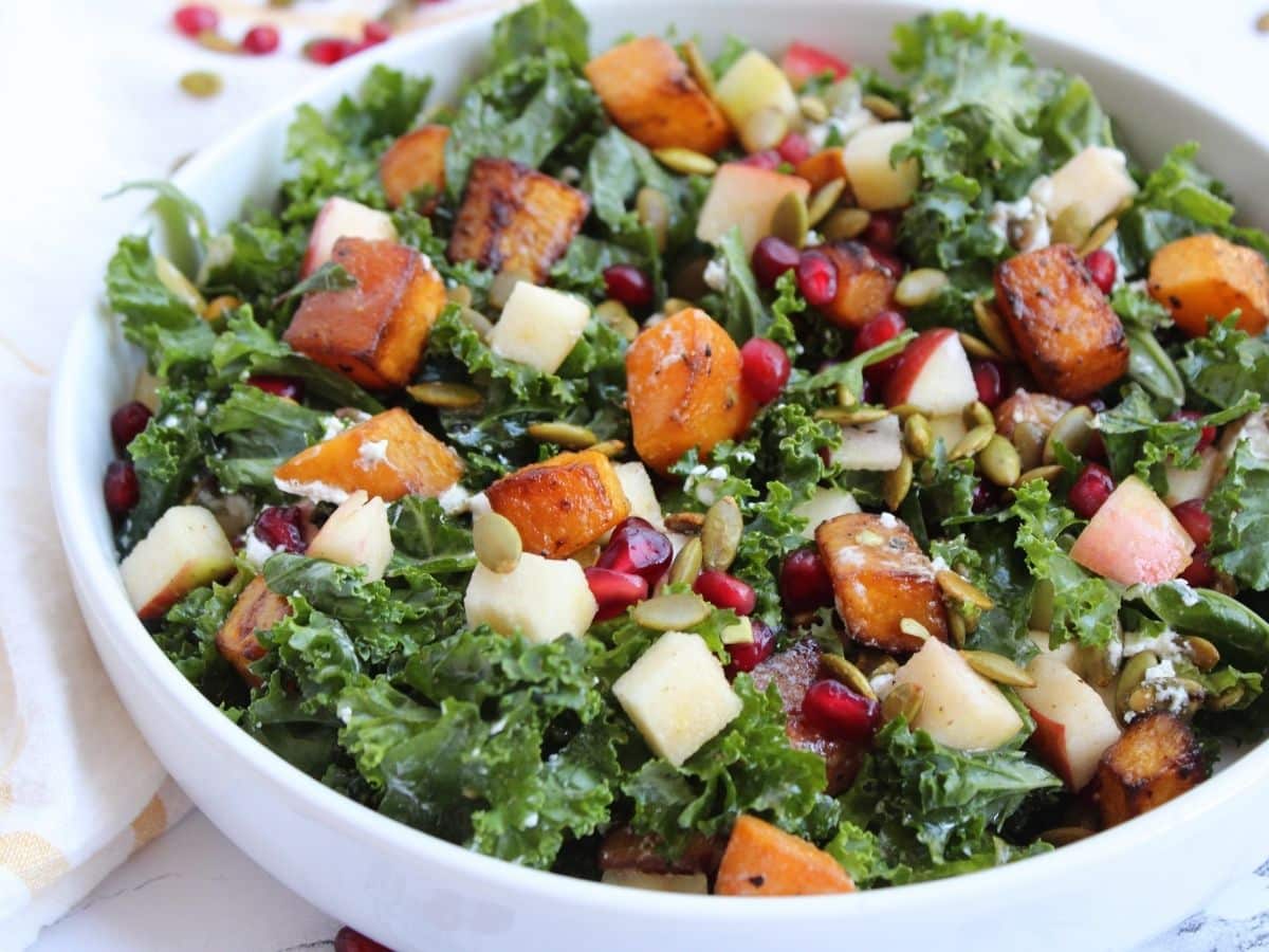 Closeup photo of a fall kale salad with butternut squash, goat cheese, pomegranate seeds, pepitas, and apple