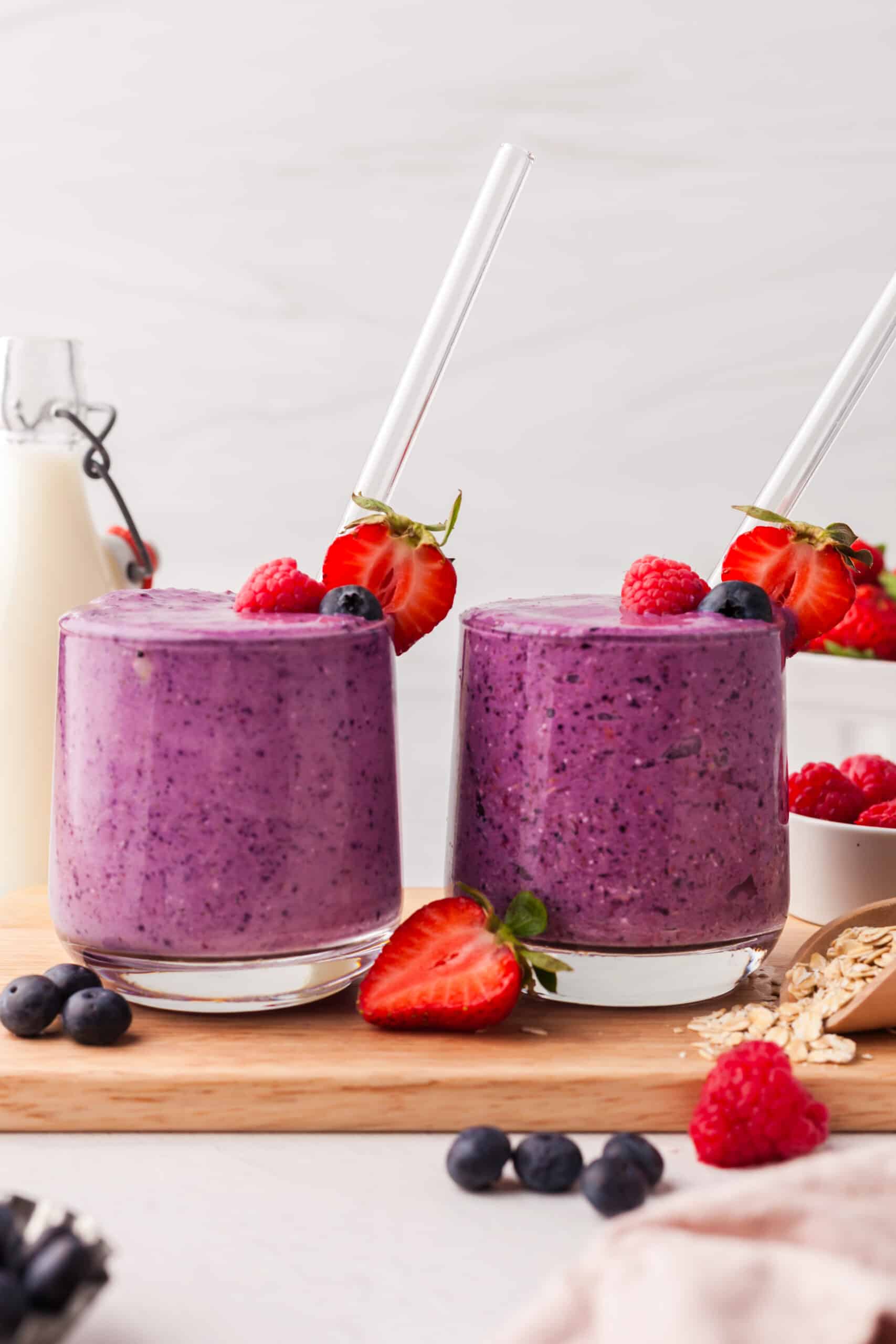 triple berry smoothies in glasses on top of a wood cutting board.