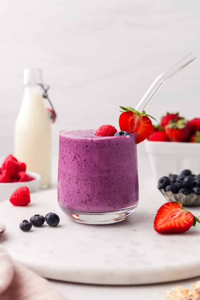 triple berry smoothie in a glass with ingredients around it.
