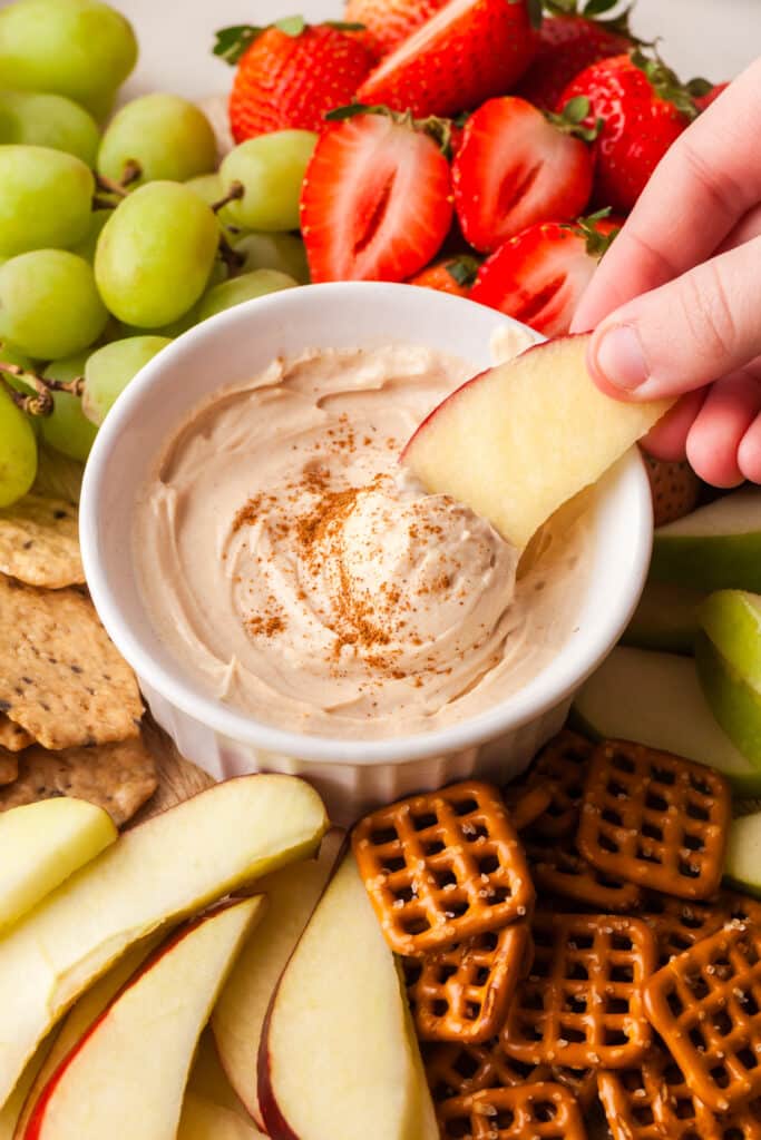 apple being hand dipped into a pb yogurt dip in bowl.