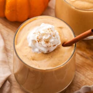 healthy pumpkin smoothie in a glass with whipped topping and cinnamon.