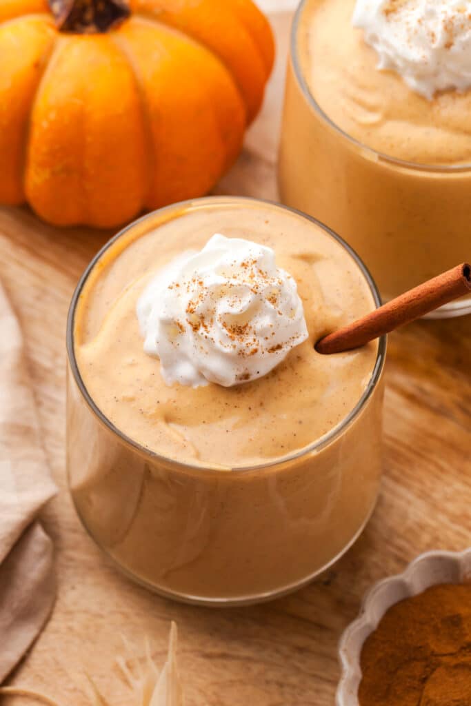 healthy pumpkin smoothie in a glass with whipped topping and cinnamon.
