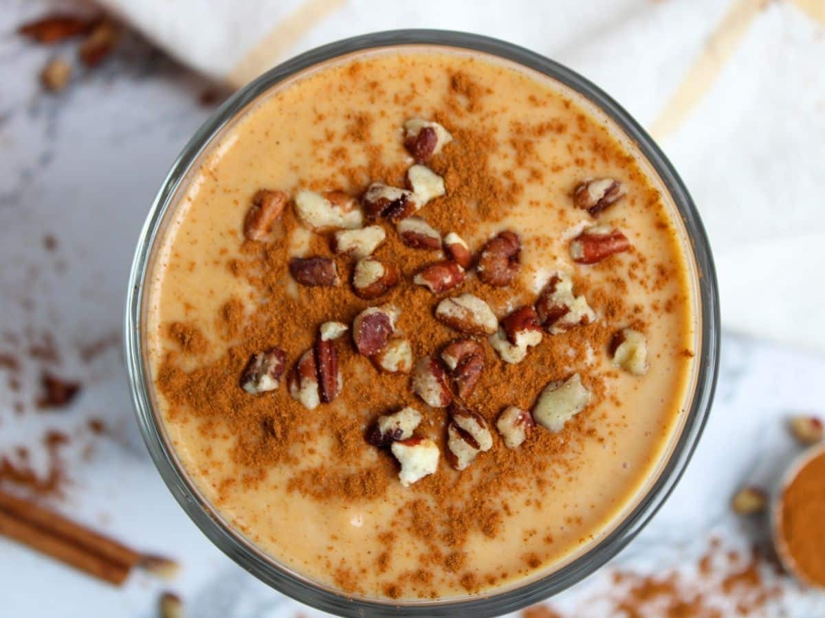 top view of healthy protein smoothie in a glass with cinnamon sprinkled on top and chopped pecans.