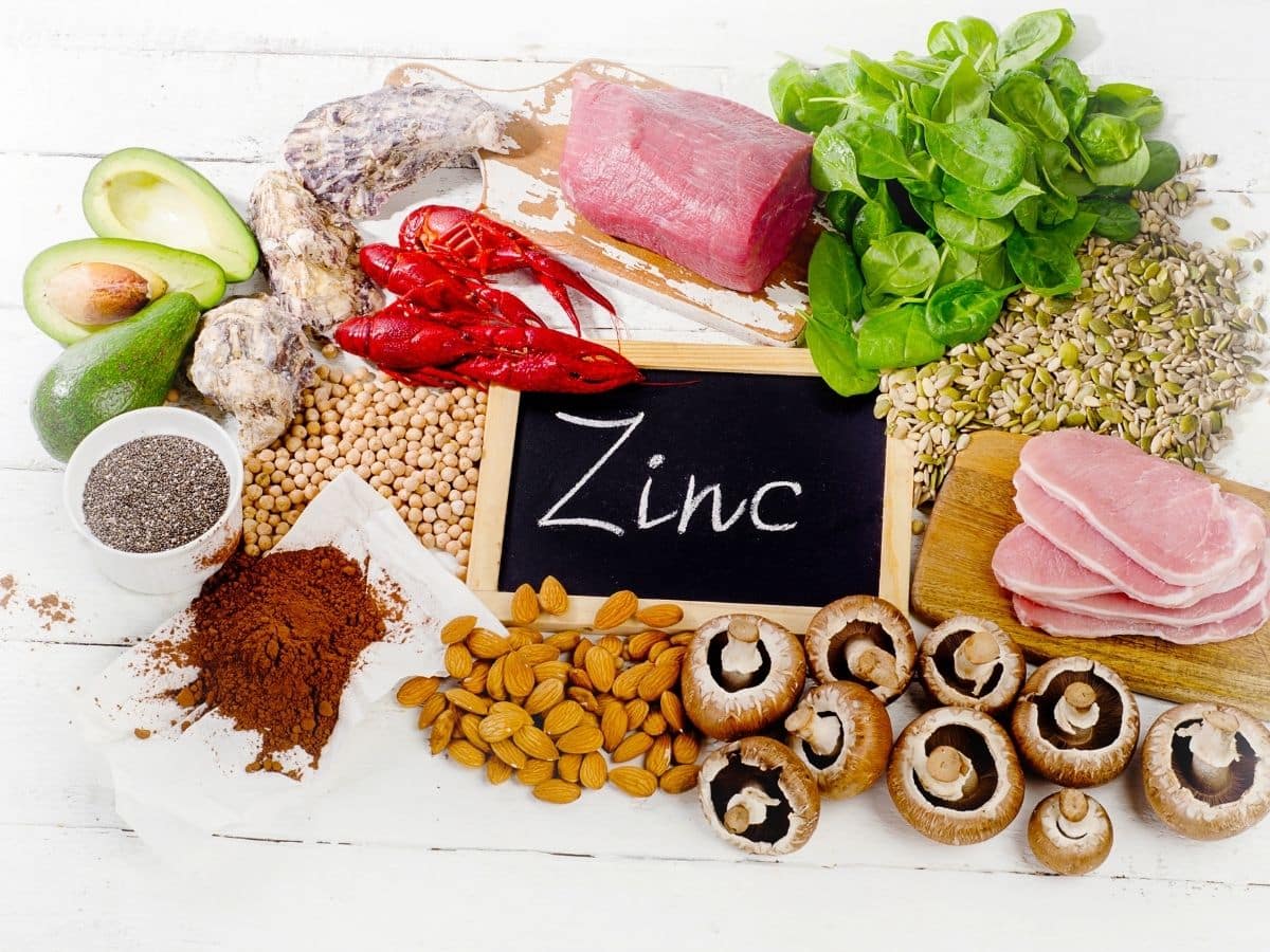 Photo of a chalkboard with the word "zinc" written out. The chalkboard is surrounded by food sources of zinc such as shellfish, beef, nuts, and legumes.