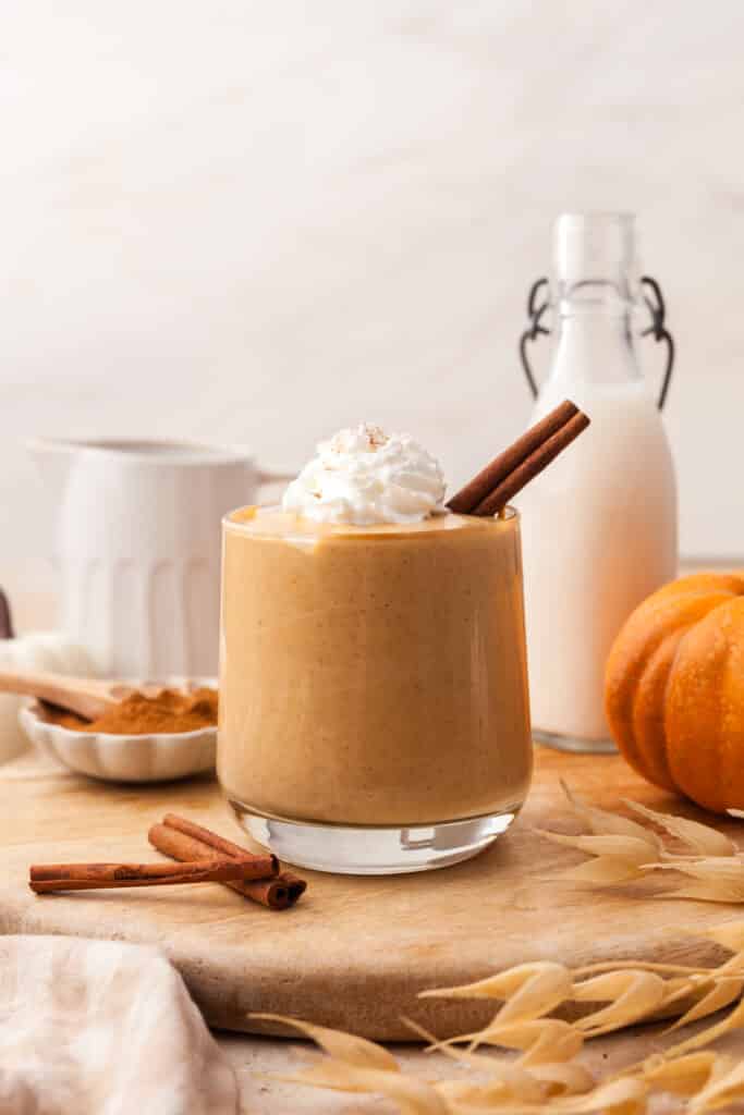 pumpkin smoothie in glass with cinnamon stick and ingredients around.