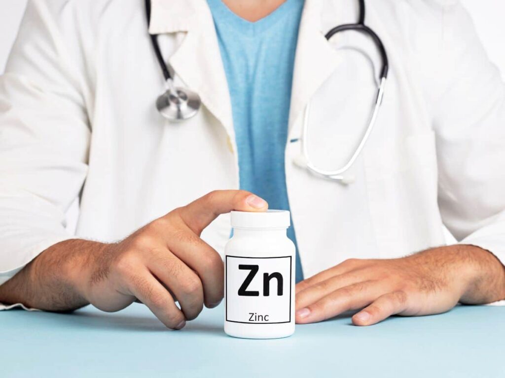 photo of a doctor in white coat with stethoscope around their neck touching a pill bottle of zinc supplement for pcos