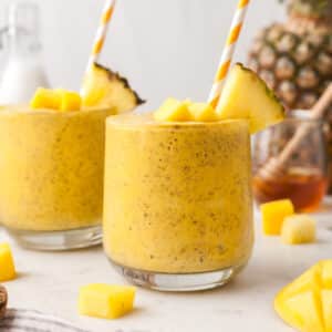 two mango kefir smoothies in glasses with fruit around it.