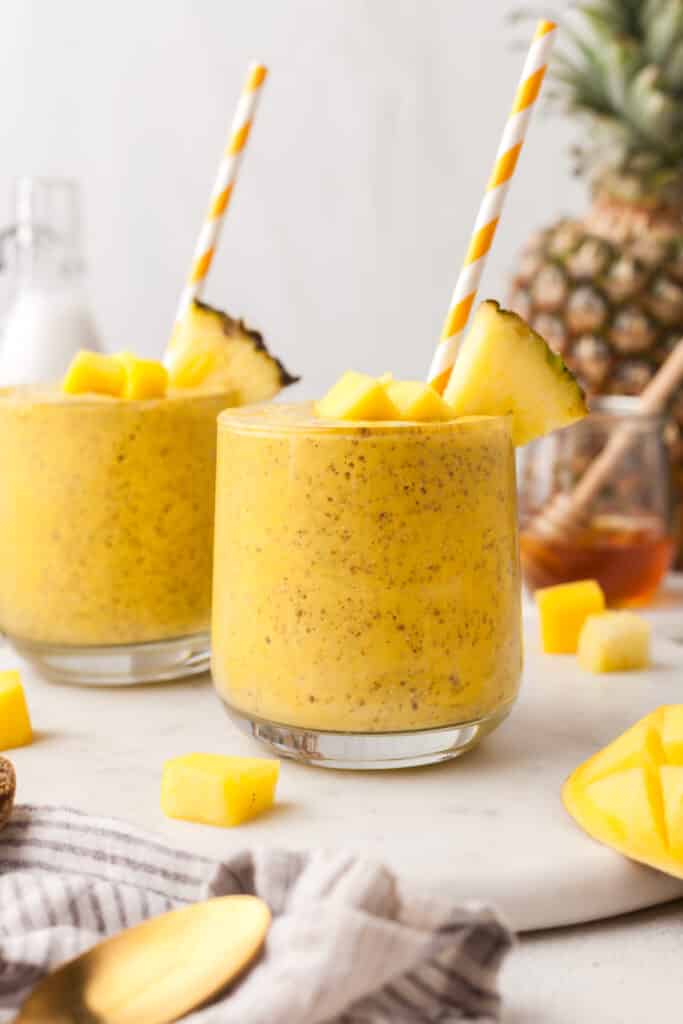 two mango kefir smoothies in glasses with fruit around it.