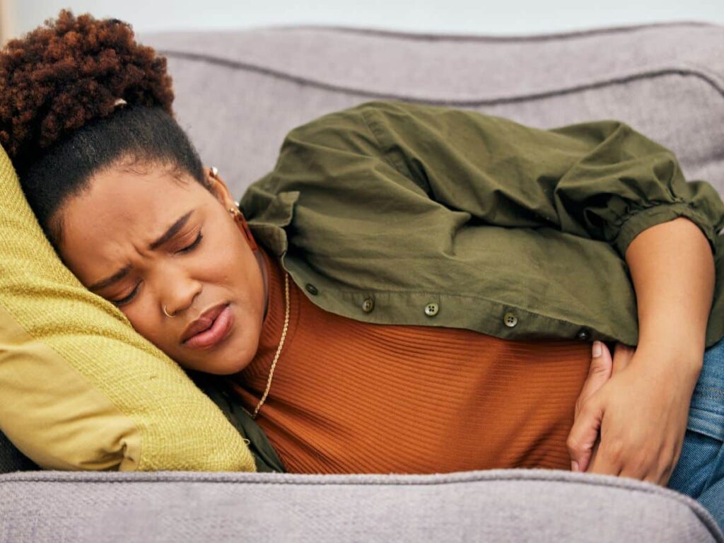 Woman laying on cough holding her stomach while grimacing. 