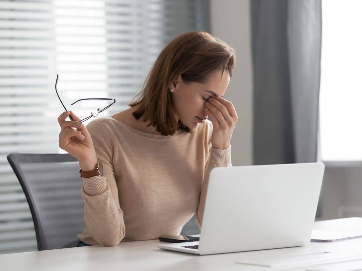 Tired woman taking her glasses off to rest while working on her laptop.