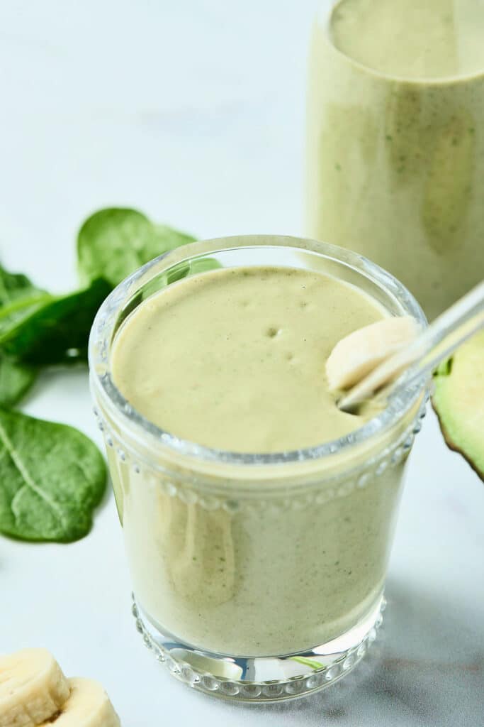 avocado peanut butter smoothie in a glass with banana topper and glass straw.