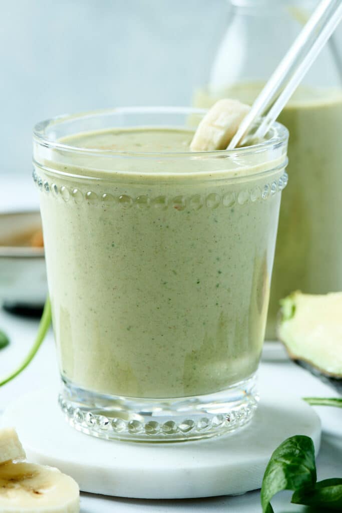 avocado peanut butter smoothie in a glass with banana slice topper and glass straw.