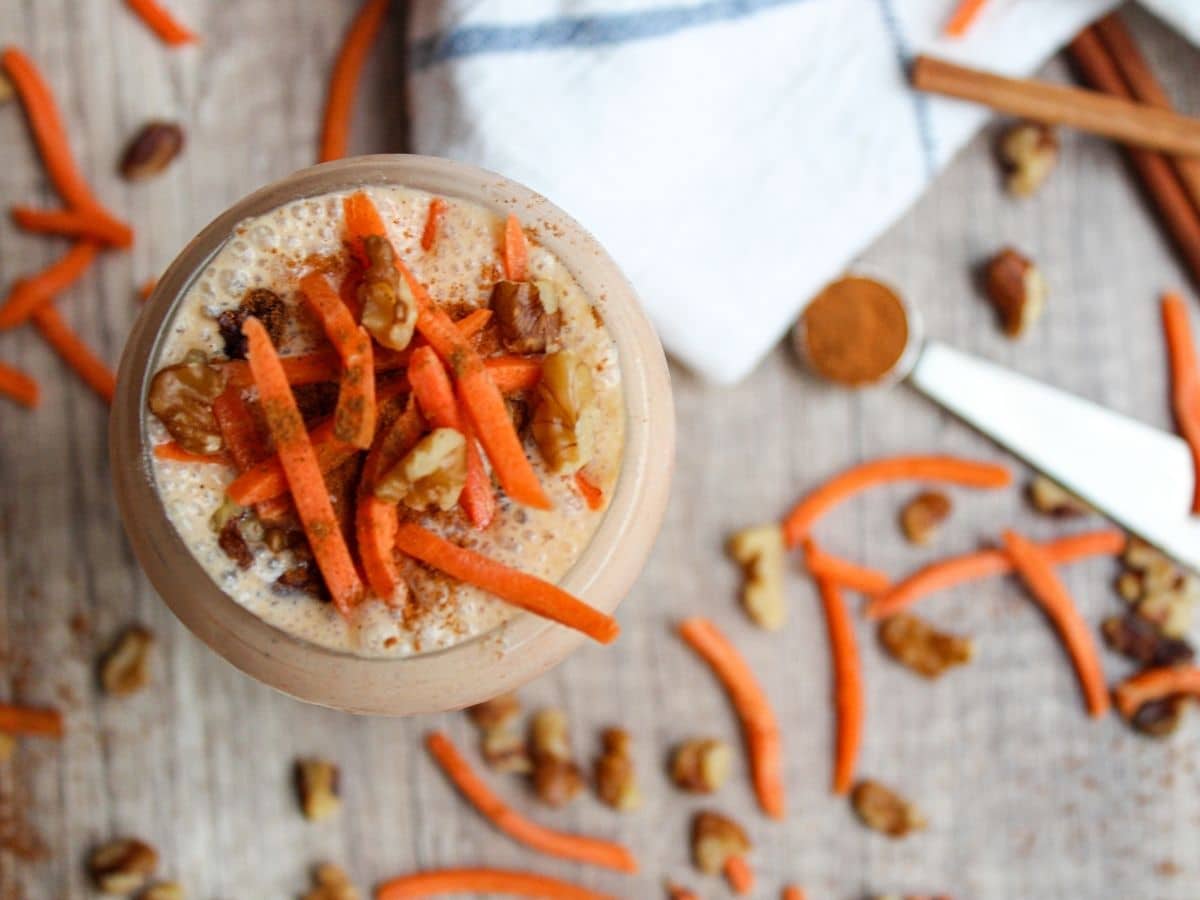 overhead shot of a carrot and banana smoothie with shredded carrots, walnuts, and cinnamon decorating the top of the smoothie.