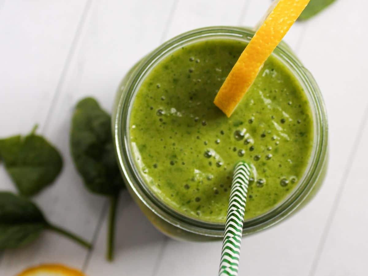 overhead view of a green smoothie with a green straw and lemon wedge on the glass rim.