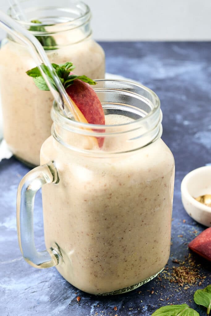 peach pineapple smoothie in a mason jar with peach slice and herbs on rim.