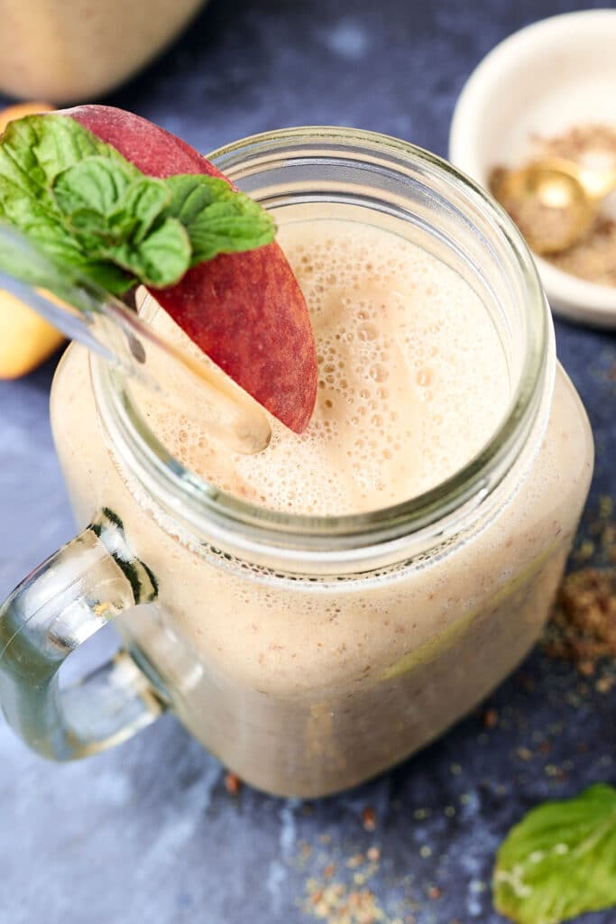 overhead view of peach pineapple smoothie in a mason jar with peach slice and herbs on rim.