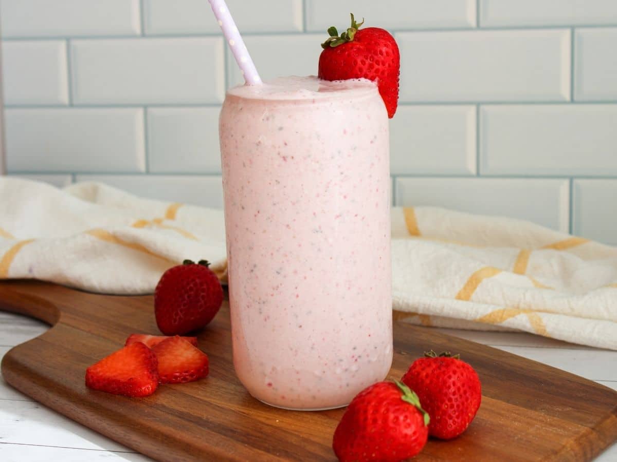 Pink strawberry cottage cheese smoothie in a tall glass with strawberries decoratively around the glass base. 