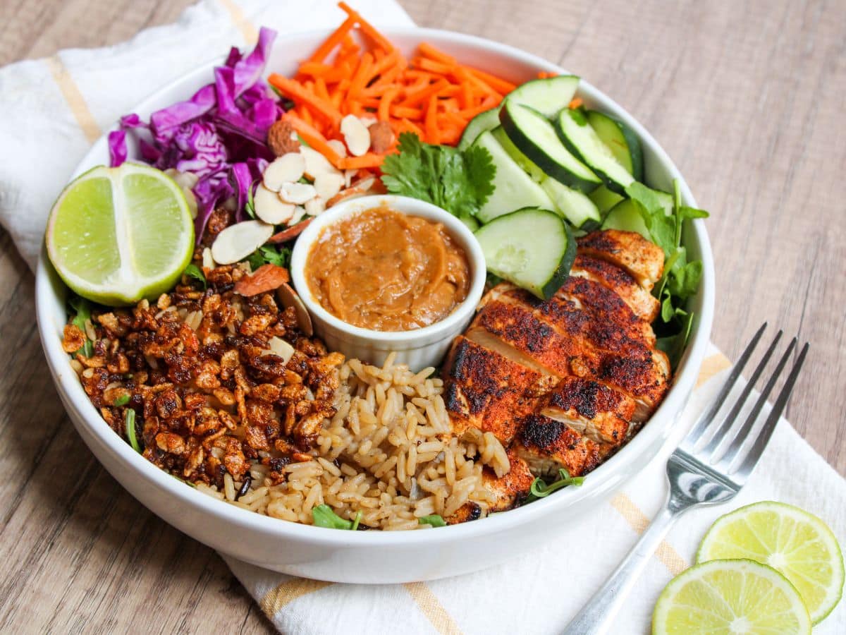 photo of a plate with crispy rice, blackened chicken, cucumbers, red cabbage, shredded carrots, slivered almonds, and spicy cashew dressing