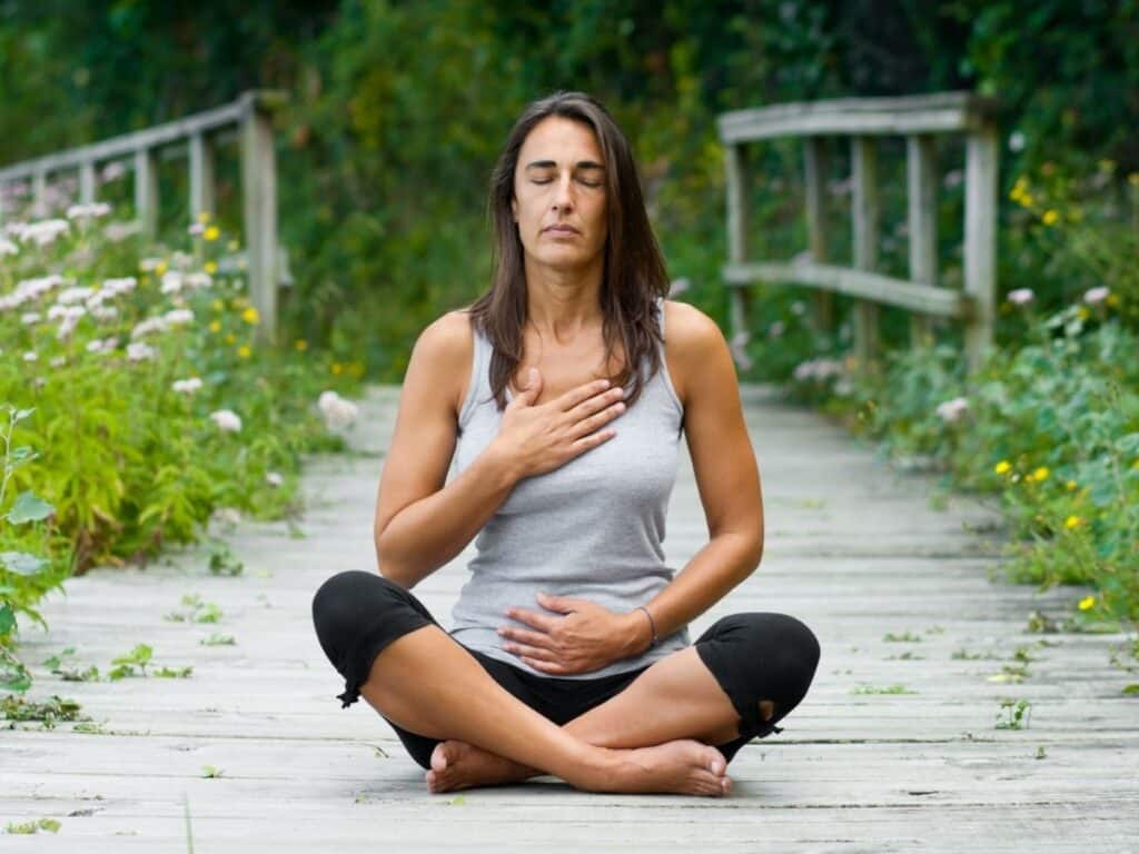 woman sitting with her hand on her chest and belly meditating.
