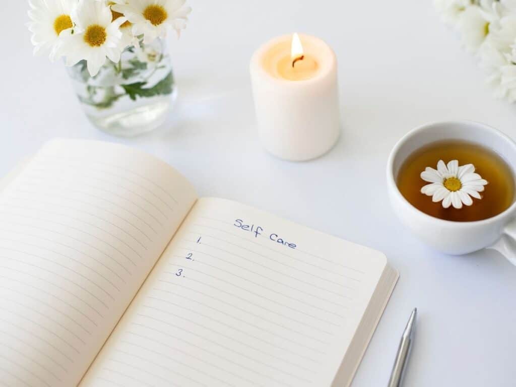 self care notebook open with a candle burning and a cup of tea.