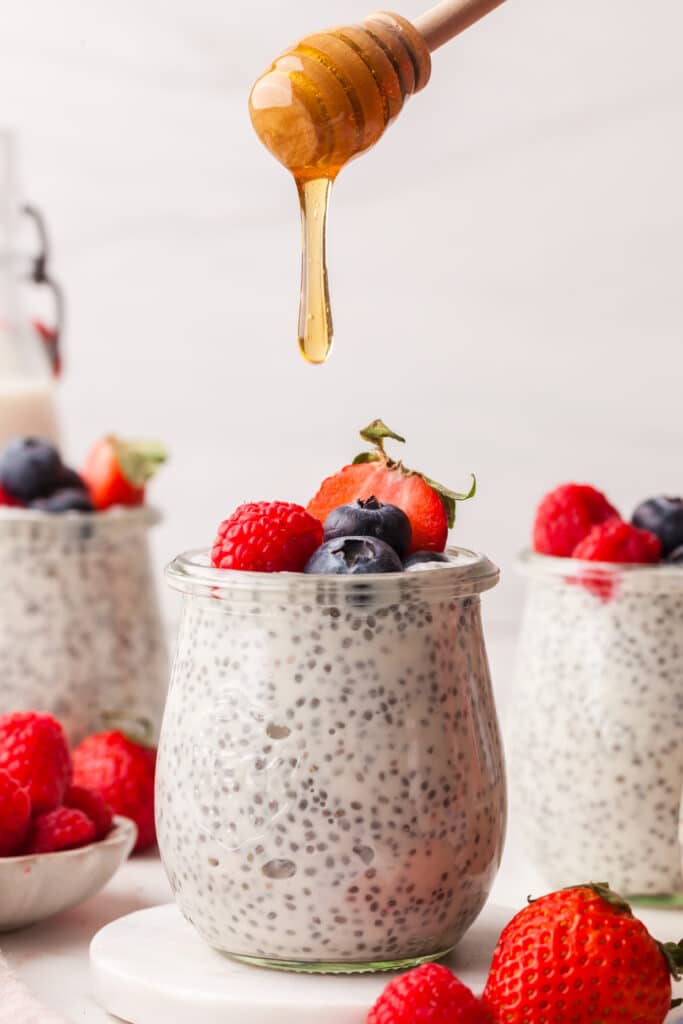 Greek yogurt chia pudding in a glass jar with berries on top and honey being drizzled on top.