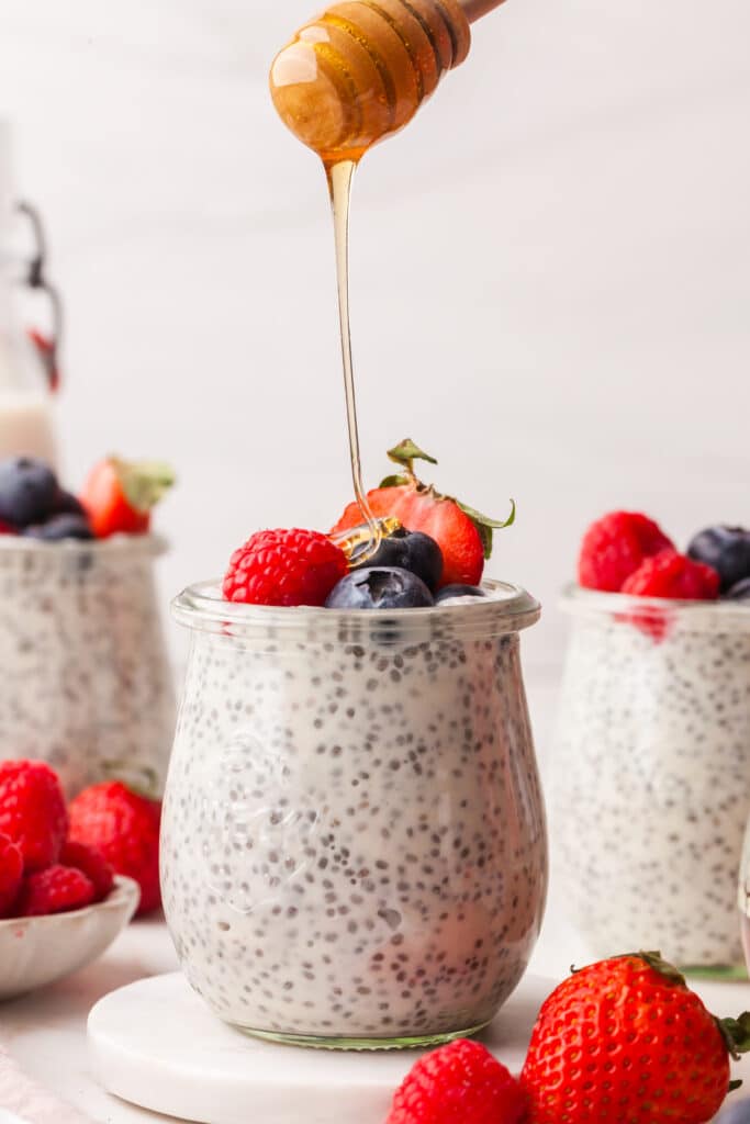 Greek yogurt chia pudding in a glass jar with berries on top and honey being drizzled on top.