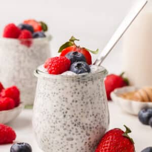 Greek yogurt chia seed pudding in a glass jar with berries and a spoon inserted.