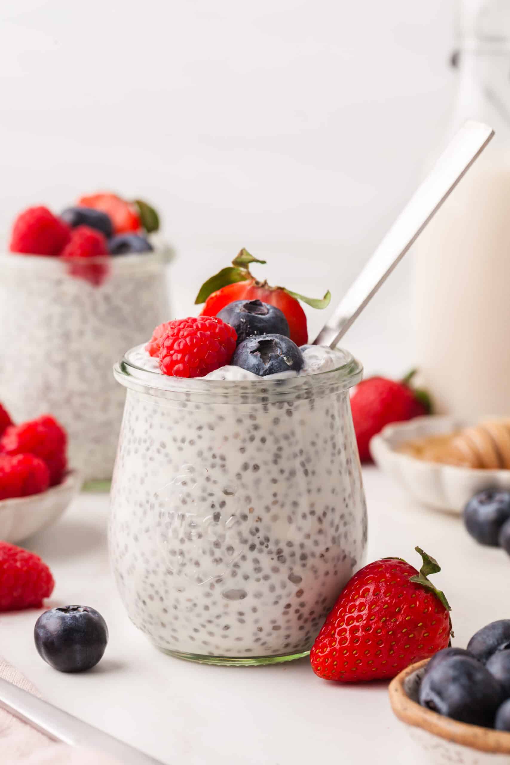 Greek yogurt chia seed pudding in a glass jar with berries and a spoon inserted.