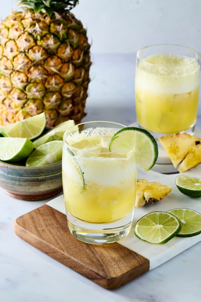 pineapple cortisol mocktail in a glass with lime garnish and ingredients surrounding it.