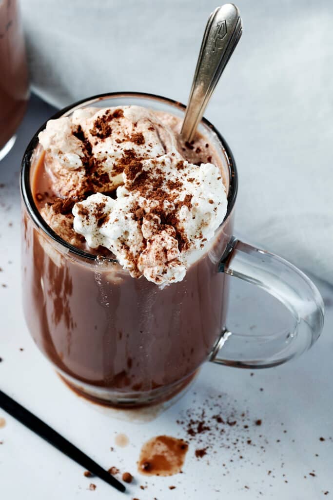 bone broth hot cocoa in a clear glass mug with whipped cream on top and a spoon inserted.