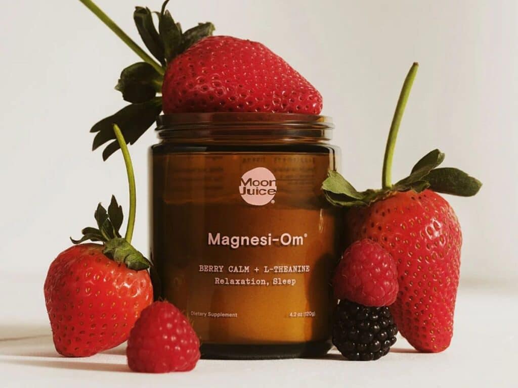 moon juice magnesi-om supplement glass jar with strawberries around it.