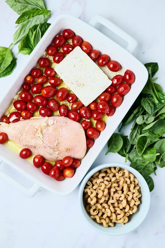 cherry tomatoes, feta cheese, and chicken in a baking dish.