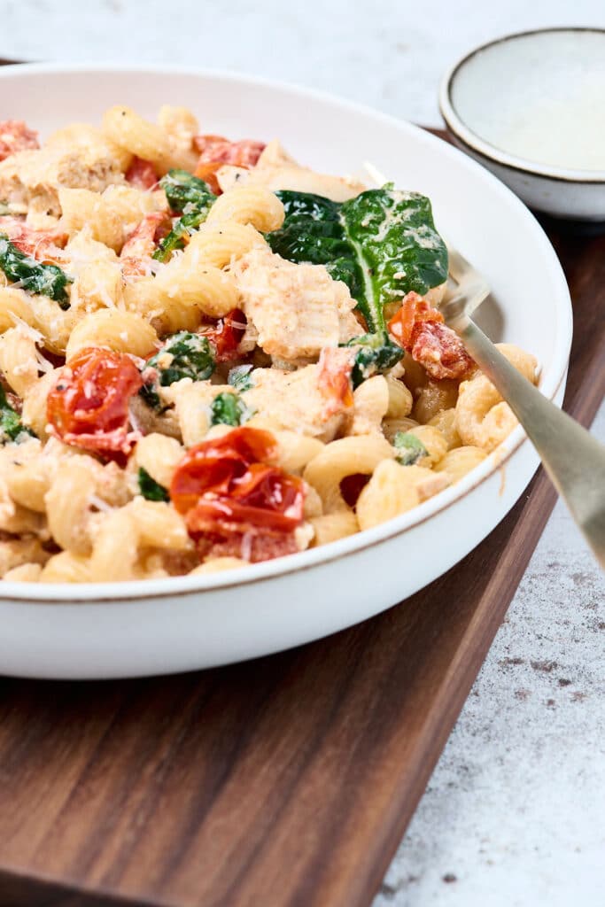baked feta pasta with chicken in a white lipped plate with utensil.