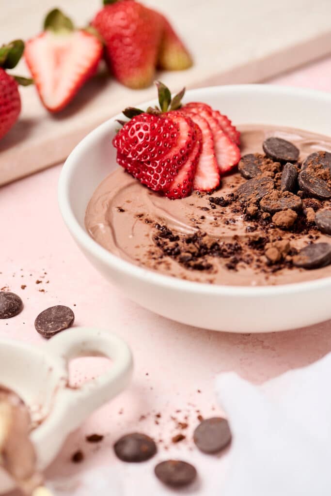 healthy brownie batter dip in a white bowl with strawberries and chocolate chips.
