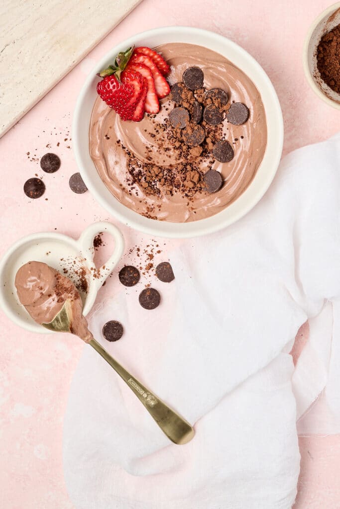 healthy brownie batter dip in a white bowl with strawberries and dark chocolate chips; a dip filled spoon next to it.