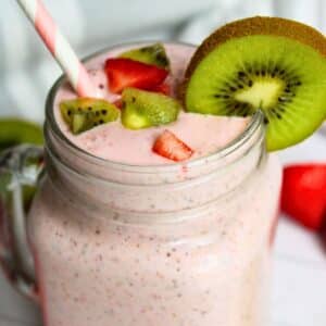 kiwi quencher tropical smoothie in a glass mug with decorative kiwi slices and strawberries around the rim.