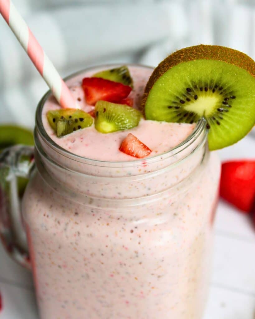 kiwi quencher tropical smoothie in a glass mug with decorative kiwi slices and strawberries around the rim.