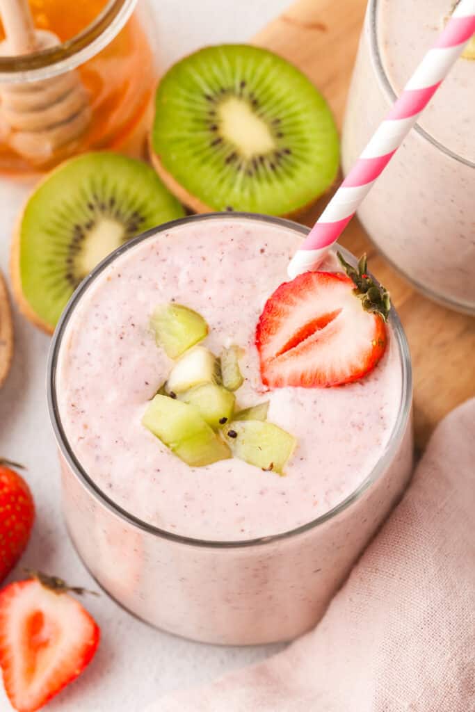 pink colored smoothie in a glass with strawberry and kiwi garnish and a straw.