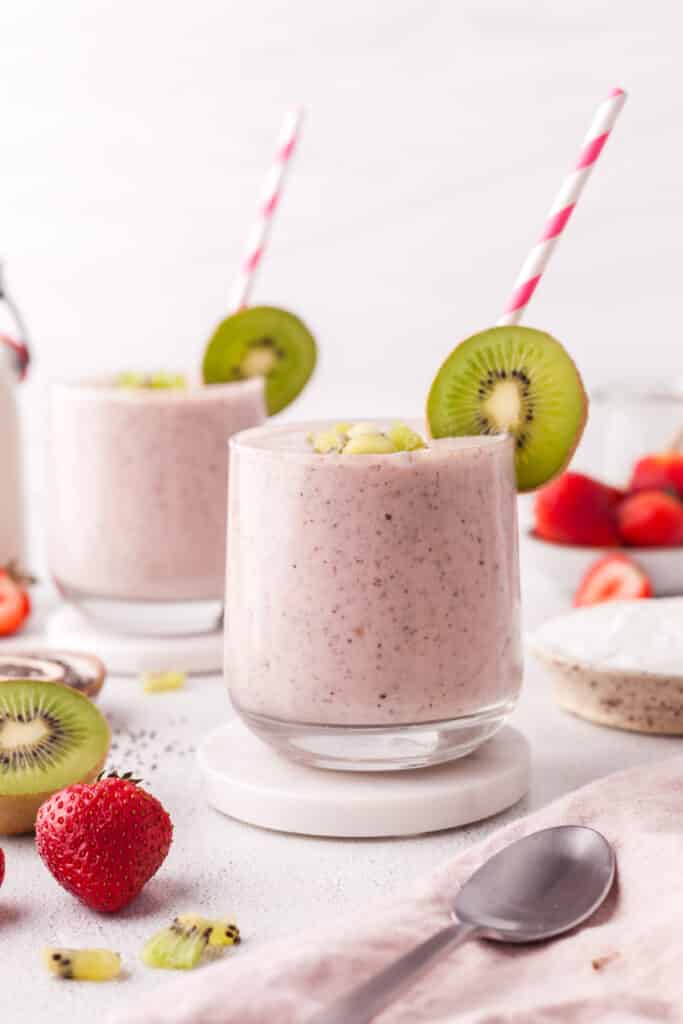 pink smoothie in glasses with kiwi garnish and striped straws.