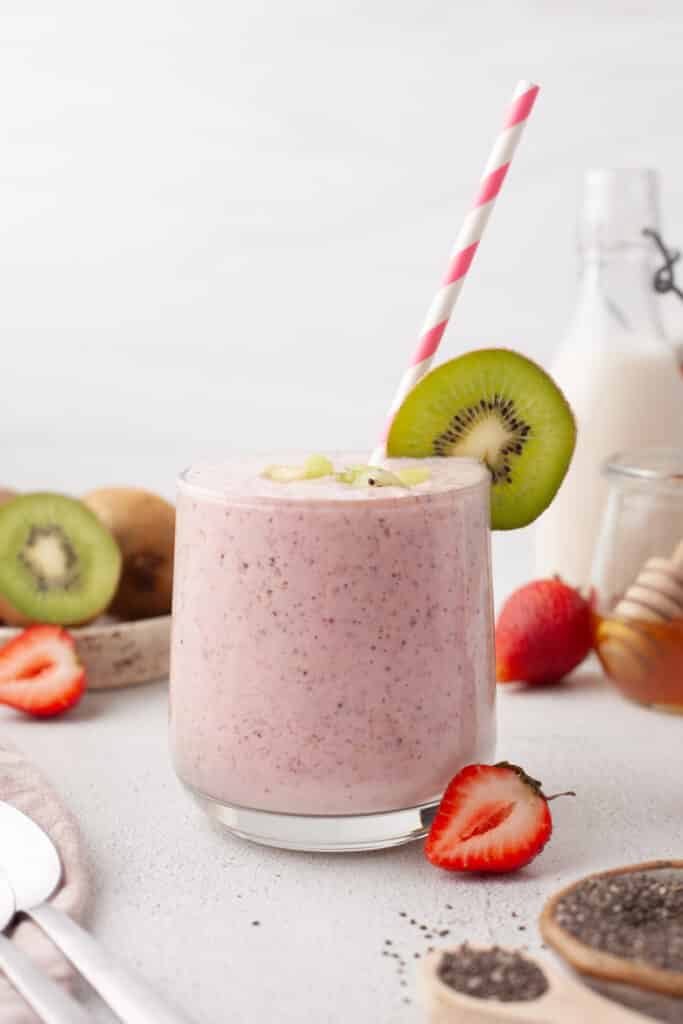 pink smoothie in glass with kiwi garnish and striped straw.
