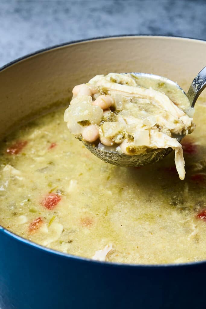 green chicken enchilada soup being scooped from pot with a ladle.