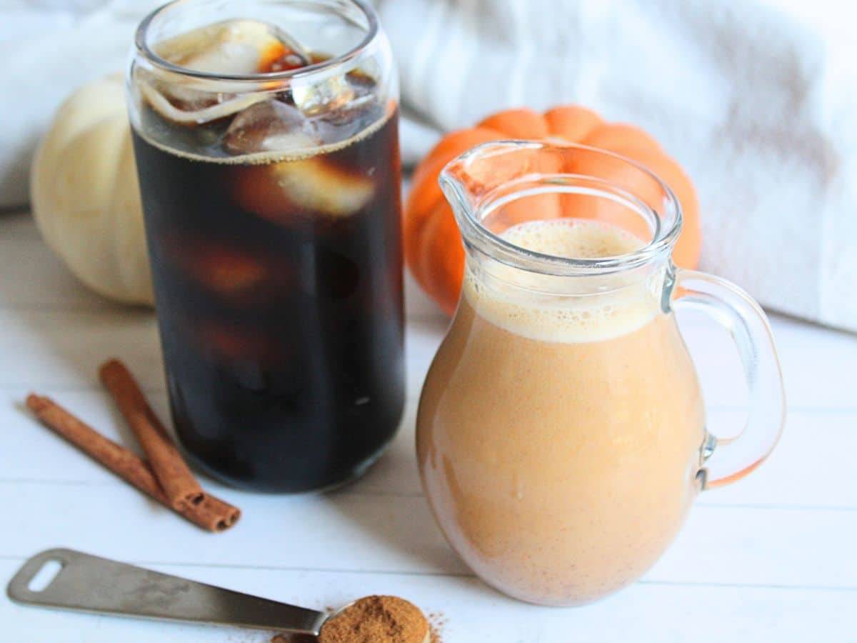homemade pumpkin spice creamer in a small glass pitcher next to an iced coffee in a glass.