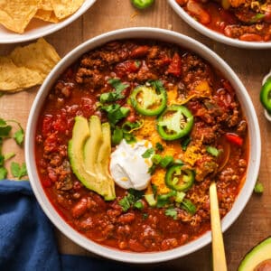 pcos friendly beef chili in a bowl topped with avocado, jalapenos, cheese, and sour cream.