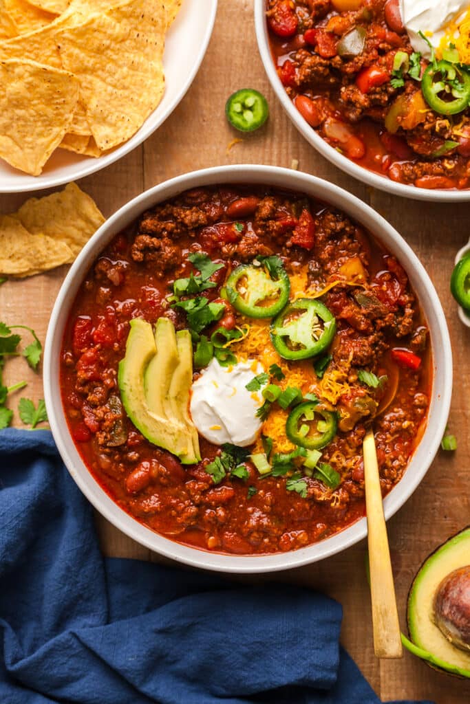 pcos friendly beef chili in a bowl topped with avocado, jalapenos, cheese, and sour cream.